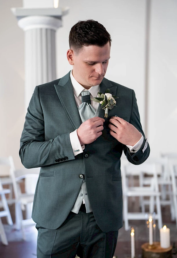 Bräutigam steckt sich voller Vorfreude den Anstecken an