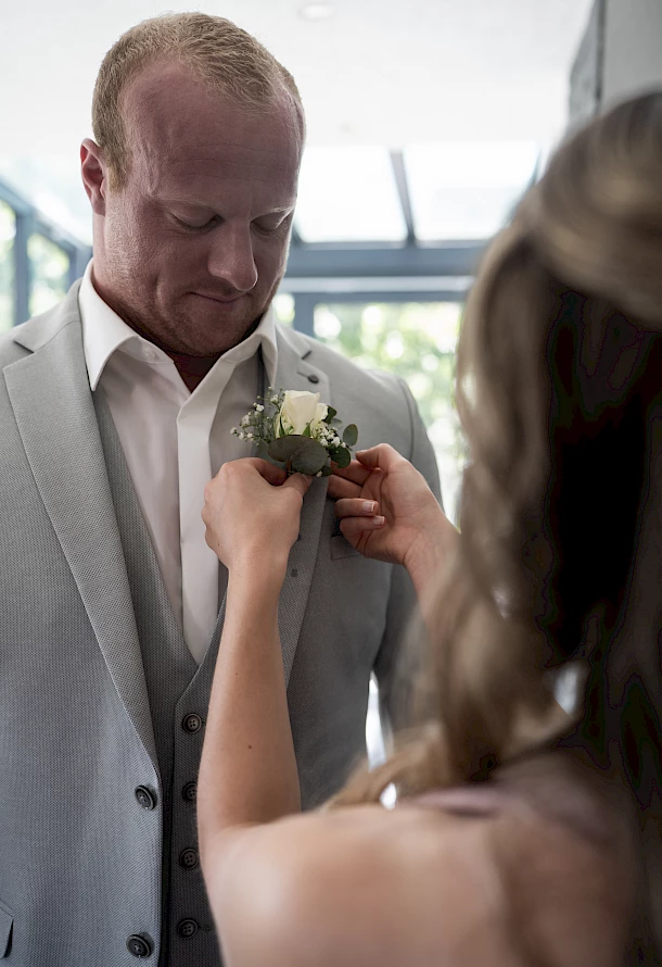 Trauzeugin steckt Bräutigam den Anstecken an