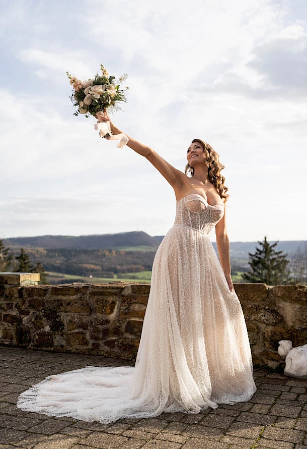 Braut im Sonnenschein mit ihrem Brautstrauß voller Freude