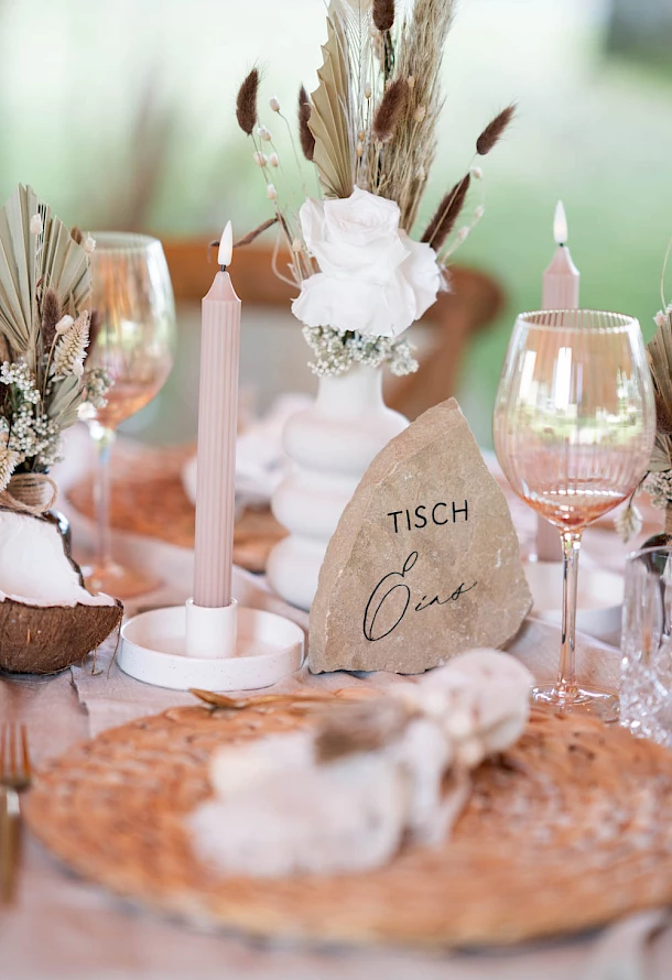 Detailaufnahme der Tischnummer auf einem Stein mit Kerzen und Trockenblumen als Dekoration