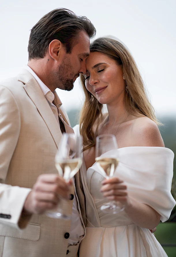 Braut und Bräutigam stoßen liebevoll mit einem Glas Sekt an
